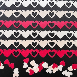 Puede incluir: Filas de guirnaldas de papel con forma de corazón en blanco, crema y rojo sobre un fondo negro. Recortes de corazón sueltos esparcidos en la parte inferior. Ideal para San Valentín o bodas.