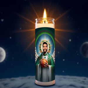 May include: A tall, lit candle with a portrait of a man in a green and white robe, holding a basketball. The candle has a green and blue design with a halo and angel wings. The background is a night sky with stars and a moon.