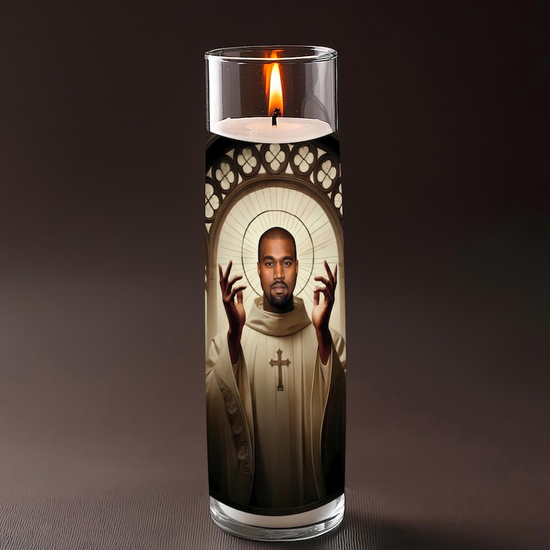 May include: A glass candle with a burning flame. The candle has an image of a man in a white robe with a cross, set against a stained-glass window design. The man is raising his hands.