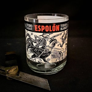 May include: A clear glass tumbler with a black and white label featuring a skeleton riding a rooster. The label reads "Espolón Tequila Blanco Puro Agave".