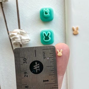 May include: Two teal blue bunny-shaped silicone molds and a small, light brown bunny-shaped polymer clay charm measuring approximately 1/2 inch in length.