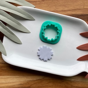 May include: A white plate with a green plastic star-shaped cookie cutter and a purple star-shaped cookie on it.