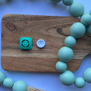 May include: A wooden cutting board with a green and white button on it. A strand of light green wooden beads is draped over the board and the edge of the table.