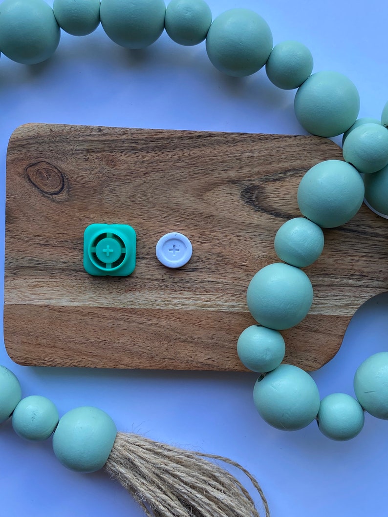 May include: A wooden cutting board with a green and white button on it. A strand of light green wooden beads is draped over the board and the edge of the table.
