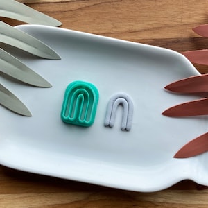 Könnte beinhalten: Zwei regenbogenförmige Tonstücke auf einem weißen Teller. Eines ist eine tealfarbene Plastikform und das andere ist ein weißes Tonstück.