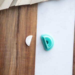 May include: Two fruit-shaped cookie cutters, one white and one turquoise blue, on a wood and white background.