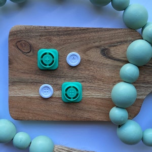 May include: A wooden cutting board with two green plastic buttons with a plus sign and four dots, and two white plastic buttons with a plus sign and four dots.