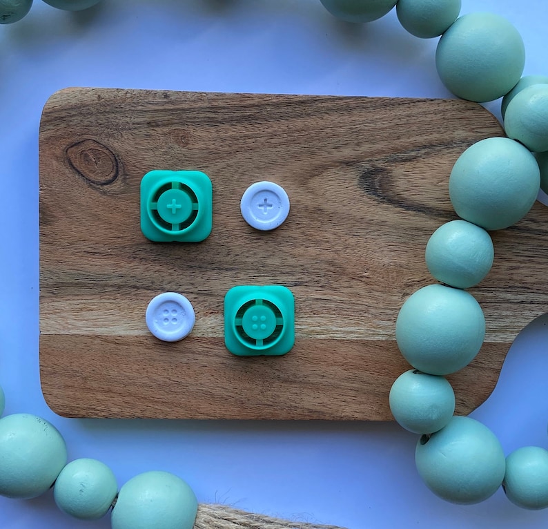 May include: A wooden cutting board with two green plastic buttons with a plus sign and four dots, and two white plastic buttons with a plus sign and four dots.