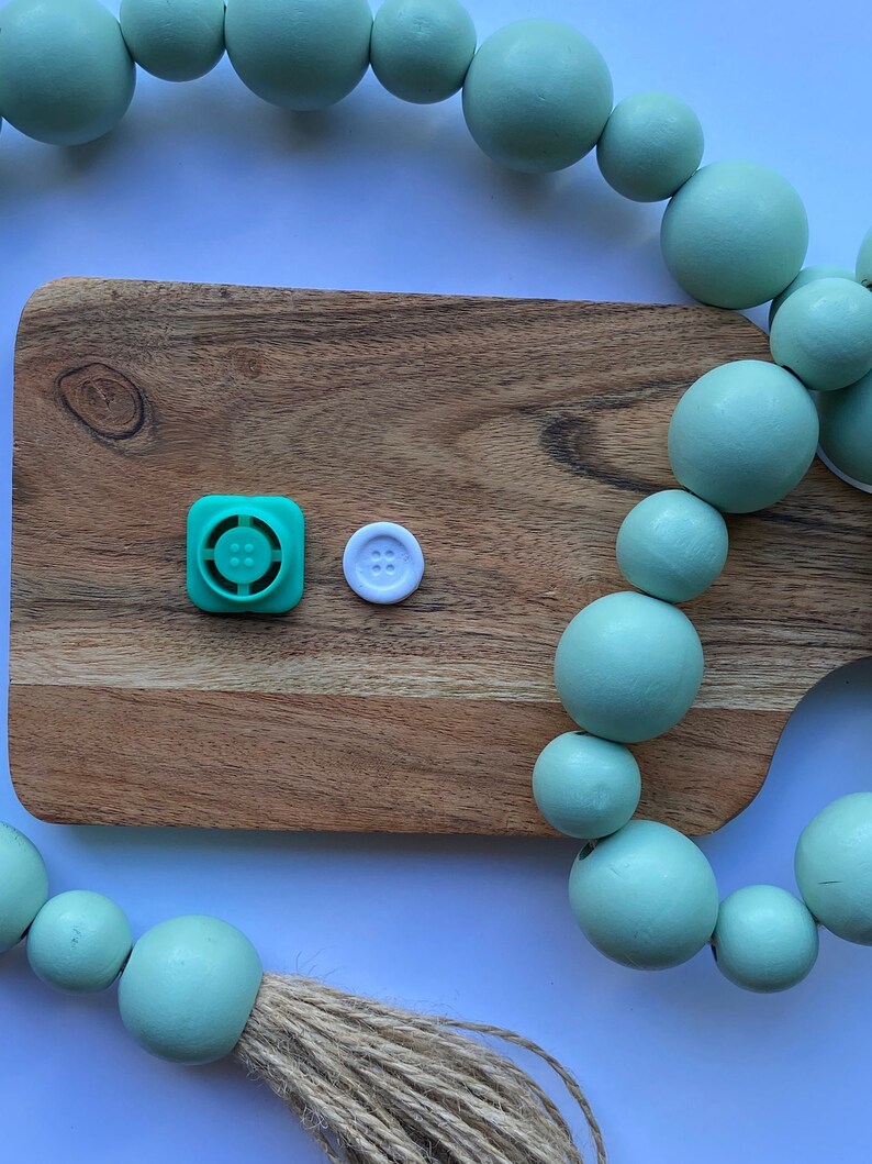 May include: A wooden cutting board with a green button and a white button on top. A string of light green wooden beads is draped over the board and the edge of the table.