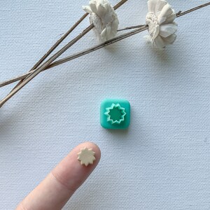 Puede incluir: Un molde de arcilla polimérica azul turquesa con un recorte en forma de estrella. Una pequeña estrella de arcilla polimérica beige está sentada en un dedo.