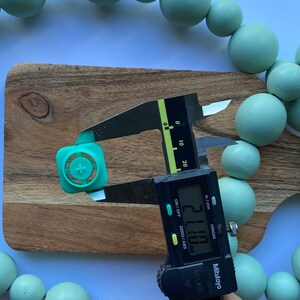 May include: A green plastic button with a plus sign in the center is being measured with a digital caliper. The caliper reads 21.10 mm.