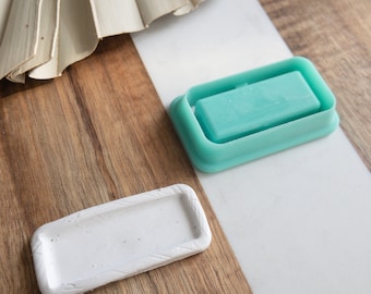 Puede incluir: Dos moldes de silicona rectangulares para hacer jabón o manualidades de resina. Un molde es blanco y el otro es azul verdoso.