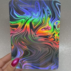 May include: A rectangular holographic sticker with a swirling, marbled design. The colors shift from blue and purple to green, yellow, and orange. The sticker has rounded corners and a glossy finish.