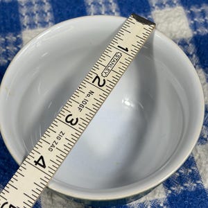 Peut inclure: Un bol en c&eacute;ramique blanche avec un int&eacute;rieur lisse, vu d'en haut. Une r&egrave;gle pliante Stanley No. 106F Zig Zag est plac&eacute;e sur l'ouverture, indiquant un diam&egrave;tre d'environ 10,2 cm pour le bord du bol.