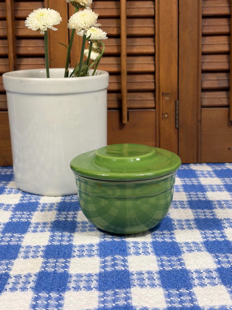 Peut inclure: Un petit beurrier en c&eacute;ramique vert brillant avec un couvercle assorti. Le r&eacute;cipient pr&eacute;sente une base arrondie lisse et un couvercle plat avec un centre l&eacute;g&egrave;rement sur&eacute;lev&eacute;, arborant une gla&ccedil;ure verte unie et &eacute;clatante sur tout l'ext&eacute;rieur.