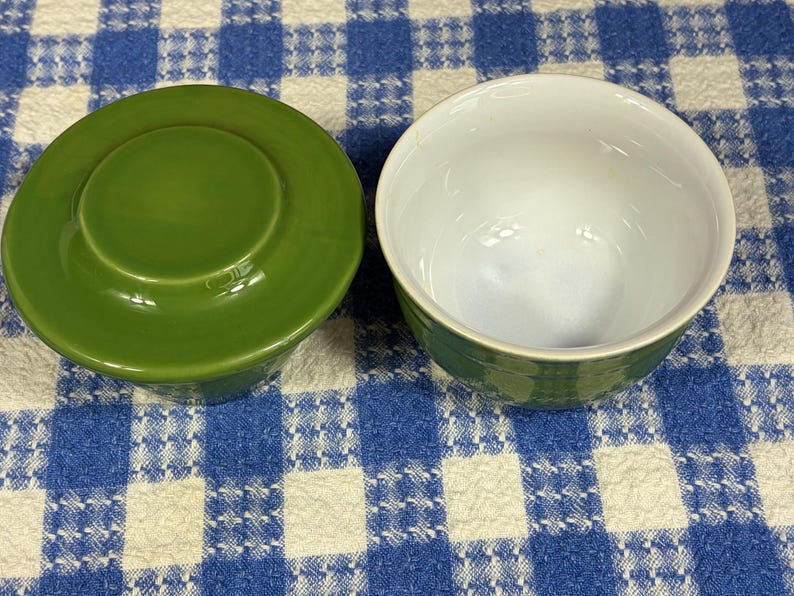 Peut inclure: Un ensemble de beurrier en c&eacute;ramique compos&eacute; de deux pi&egrave;ces avec un ext&eacute;rieur vert olive uni. Une pi&egrave;ce est un couvercle circulaire avec une poign&eacute;e centrale sur&eacute;lev&eacute;e, et l'autre est un bol ouvert et vide avec un int&eacute;rieur blanc brillant et lisse.