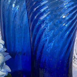 Pu&ograve; includere: Due alti bicchieri di vetro blu cobalto con un design testurizzato e a spirale. I bicchieri hanno un'estetica vintage e sono parzialmente visibili, mostrando il loro motivo decorativo unico. La tonalit&agrave; blu &egrave; ricca e vibrante.