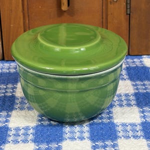 Peut inclure: Un bol rond en c&eacute;ramique vert gazon brillant avec un couvercle assorti. Le bol pr&eacute;sente une silhouette lisse et incurv&eacute;e avec une fine cr&ecirc;te horizontale pr&egrave;s du bord sup&eacute;rieur, offrant un design &eacute;pur&eacute; et fonctionnel pour le rangement ou le service.