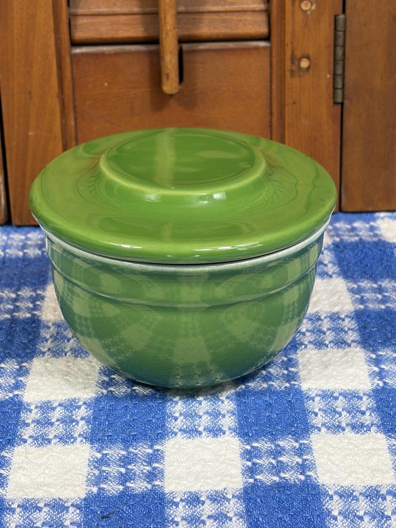 Peut inclure: Un bol rond en c&eacute;ramique vert gazon brillant avec un couvercle assorti. Le bol pr&eacute;sente une silhouette lisse et incurv&eacute;e avec une fine cr&ecirc;te horizontale pr&egrave;s du bord sup&eacute;rieur, offrant un design &eacute;pur&eacute; et fonctionnel pour le rangement ou le service.