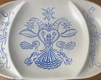 Può includere: Vassoio ovale in ceramica bianco sporco con un disegno di uccelli e fiori blu. Il centro presenta due uccelli uno di fronte all'altro, con un disegno a forma di cuore tra loro. I bordi hanno motivi floreali e di foglie.