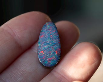 Splendido opale australiano doppietto da 11 carati, con supporto in pietra di ferro. Opale scuro a forma di goccia lunga con vivaci tonalità di rosso, arancione, verde e blu.