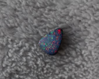 Doppietta di opale australiano da 0,95 ct, piccola, luminosa e bellissima! Supporto in vetro nero, tonalità blu, rosse, arancioni, gialle e verdi.