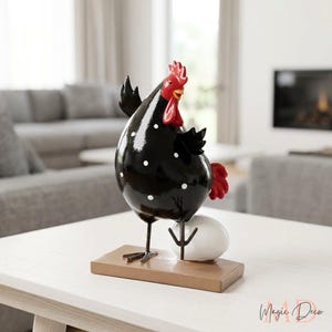 May include: A black chicken figurine with white polka dots, a bright red comb and wattle, and a red tail. The chicken stands on a rectangular brown base next to a smooth white egg. The figure has thin metal legs and a glossy finish.