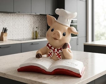 May include: A light tan ceramic pig figurine wearing a white chef hat and a red and white chequered scarf. The pig is resting its chin on one hoof while looking at an open white book with a red cover that has embossed script text on the pages.