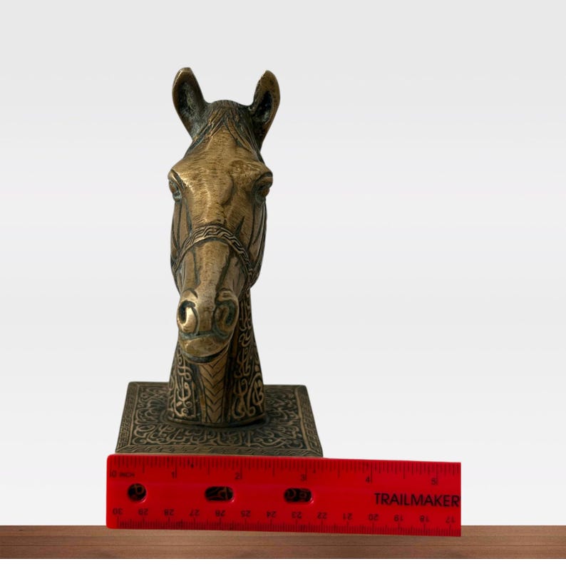 May include: A bronze horse head sculpture with intricate details, including a bridle and decorative base. The sculpture measures approximately 6 inches in height, as indicated by the ruler in the image. The horse head is a decorative item.