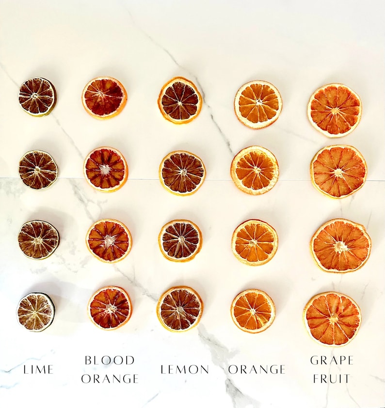 May include: Dried citrus fruit slices arranged in rows on a white marble background. The slices are labeled as lime, blood orange, lemon, orange, and grape fruit.