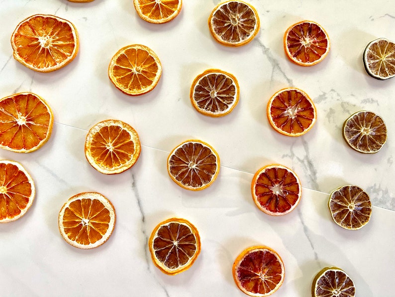May include: A collection of dried orange and lime slices arranged on a white marble surface. The citrus slices are a variety of colors, including yellow, orange, and brown.