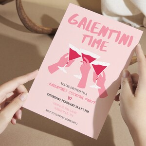 May include: Pink invitation card with the text "Galentini Time" in white lettering. The card features a graphic of three hands holding pink martini glasses with red liquid. The text below the graphic reads "You're invited to a Galentines Cocktail Party" with a pink heart symbol. The date and time of the party are listed as "Thursday February 13 at 7 PM" and the location is "1400 Gal Pal Lane, Nashville, TN". The RSVP information is "RSVP to Cupid by February 1."