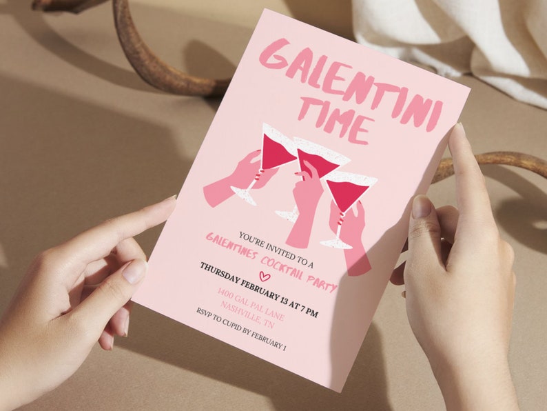May include: Pink invitation card with the text "Galentini Time" in white lettering. The card features a graphic of three hands holding pink martini glasses with red liquid. The text below the graphic reads "You're invited to a Galentines Cocktail Party" with a pink heart symbol. The date and time of the party are listed as "Thursday February 13 at 7 PM" and the location is "1400 Gal Pal Lane, Nashville, TN". The RSVP information is "RSVP to Cupid by February 1."