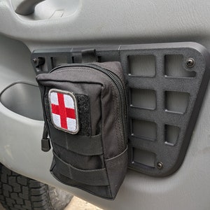 May include: A black first aid kit with a red cross patch is attached to a black metal grid mounted on a gray car door.