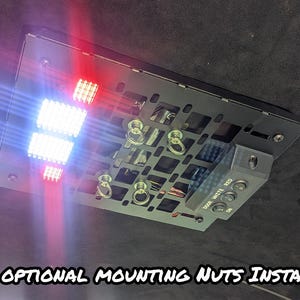 Może przedstawiać: Czarny metalowy panel ze zintegrowanymi światłami LED, w tym białymi i czerwonymi światłami. Panel posiada różne punkty montażowe oraz panel sterowania z przyciskami. Tekst na dole brzmi "*WITH OPTIONAL MOUNTING NUTS INSTALLED".