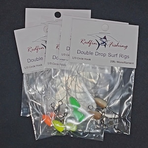 May include: Three packages of Redfin Double Drop Surf Rigs fishing tackle. Each package contains a 1/0 circle hook, 20lb monofilament line, and a green, orange, and brown bead. The packages are labeled "Redfin Fishing" and "Double Drop Surf Rigs".