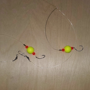 May include: Two fishing rigs with yellow and red beads, each with a hook at the end.