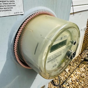 May include: A clear, rectangular electric meter with a digital display, mounted on a light gray surface. A copper coil surrounds the meter. The meter has text that reads "YORK ELECTRIC CO-OP".