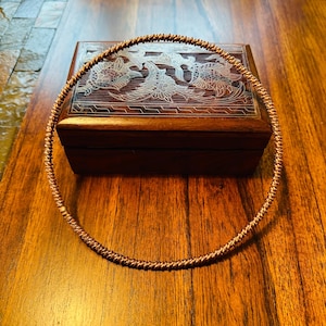 May include: A copper wire choker necklace with a twisted design. The necklace is lying on a wooden surface.