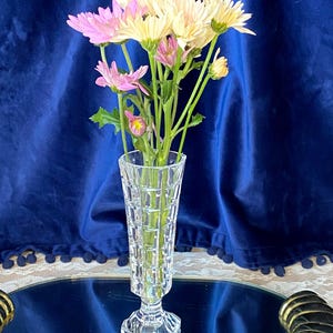 Puede incluir: Un jarrón de cristal transparente con un ramo de flores rosas y crema. El jarrón está sobre una bandeja de espejo con asas doradas, contra un telón de fondo azul oscuro. Aproximadamente 20 cm de altura.