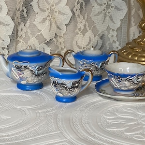 May include: A miniature blue and white porcelain tea set with gold trim. The set includes a teapot, sugar bowl, creamer, teacup, and saucer. Each piece is decorated with a detailed Asian-inspired design.