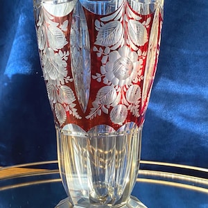 May include: A clear glass vase with a red interior and etched floral designs. The vase has a faceted base and a flared top. The floral pattern includes detailed leaves and flowers, creating a decorative piece.