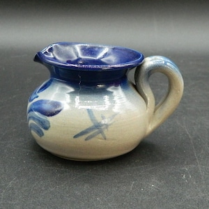 May include: A small, ceramic pitcher with a rounded body and a curved handle. The rim and interior are a deep blue, with a lighter blue and beige body. Decorative blue brushstrokes and a dragonfly design adorn the exterior.