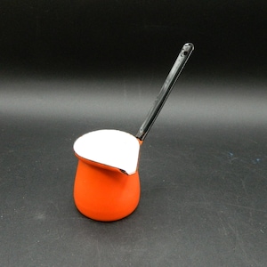 Könnte beinhalten: Eine orangefarbene und weiße Emaille-Kaffeekanne mit einem langen schwarzen Griff. Die Kanne hat einen abgerundeten Boden und einen weißen Rand. Der Griff ist an der Seite der Kanne befestigt und biegt sich nach oben. Die Kanne ist wahrscheinlich Vintage.