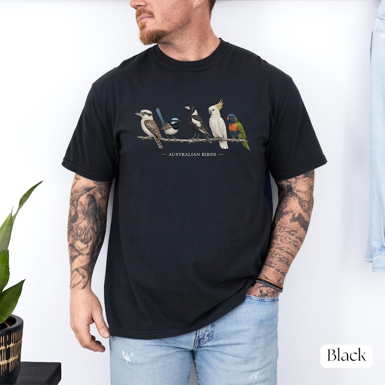 Puede incluir: Una camiseta negra de manga corta con un estampado gr&aacute;fico de cinco aves australianas posadas en una rama. La ilustraci&oacute;n incluye un cucaburra, una ratona australiana, un verdugo p&iacute;o, una cacat&uacute;a y un lori, con el texto AUSTRALIAN BIRDS.