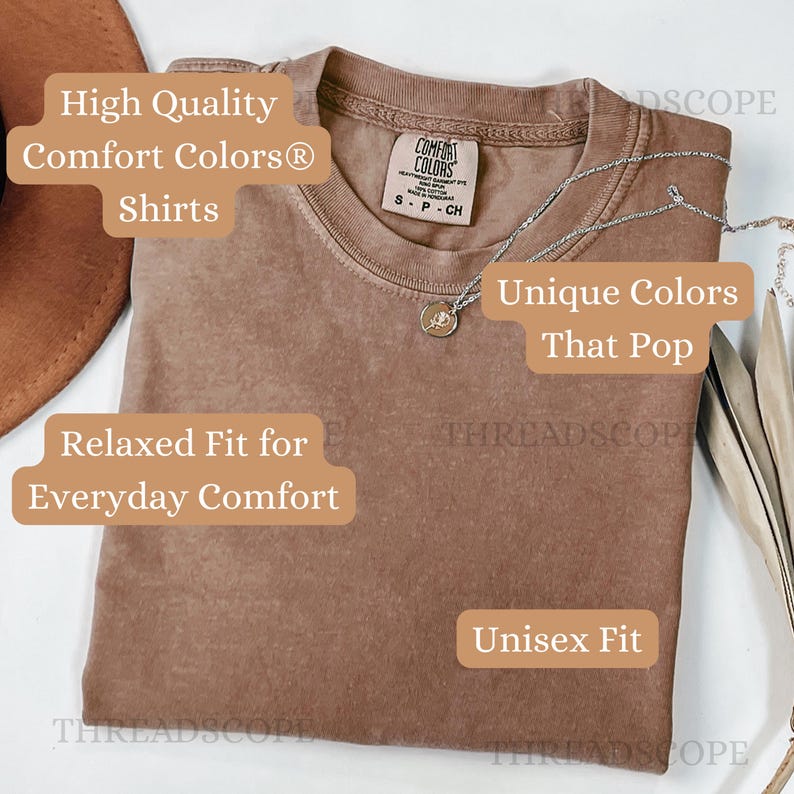 Puede incluir: Una camiseta marr&oacute;n lisa con cuello redondo y una etiqueta de la marca Comfort Colors en el interior del cuello. Un collar de cadena plateada fina con un peque&ntilde;o colgante circular descansa sobre la tela. La camiseta tiene un corte holgado.