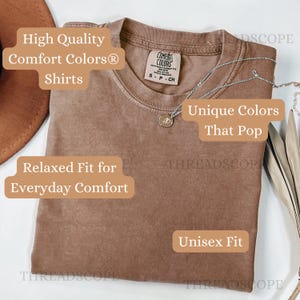 May include: A brown Comfort Colors t-shirt with the text "High Quality Comfort Colors Shirts", "Relaxed Fit for Everyday Comfort", "Unique Colors That Pop", and "Unisex Fit". A silver necklace with a pendant is draped across the shirt.