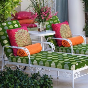 May include: Two white metal lounge chairs with green and white polka dot cushions and orange throw pillows. The chairs are on a patio with green plants.