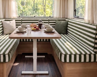 May include: A dining area inside a camper featuring a wooden table with a white adjustable base, surrounded by U-shaped bench seating upholstered in green and white striped fabric, with light-colored curtains and wood cabinetry.
