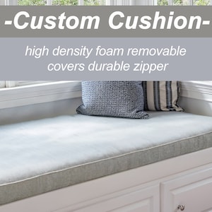 May include: A light gray window seat cushion with a white border. The cushion is made of high-density foam and has a removable cover with a durable zipper. The cushion is placed on a white window seat with two drawers. The text on the cushion reads: -Custom Cushion- high density foam removable covers durable zipper